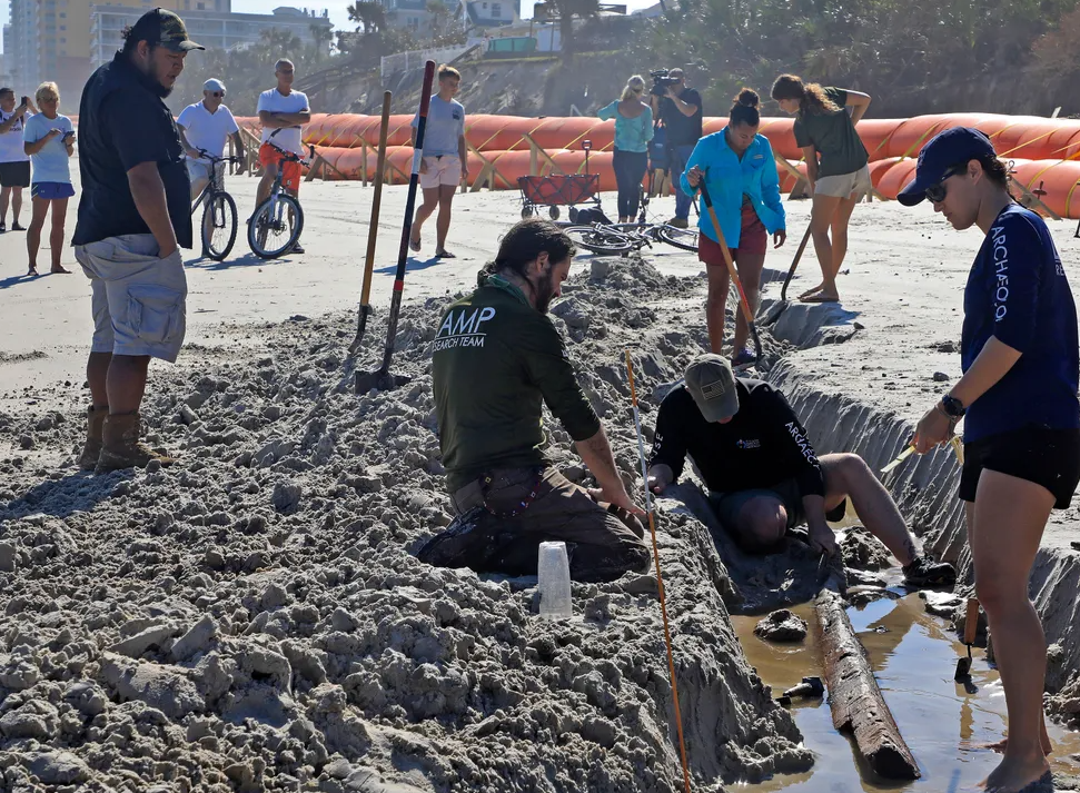 archaeologists unearthing a shipwreck on a beach