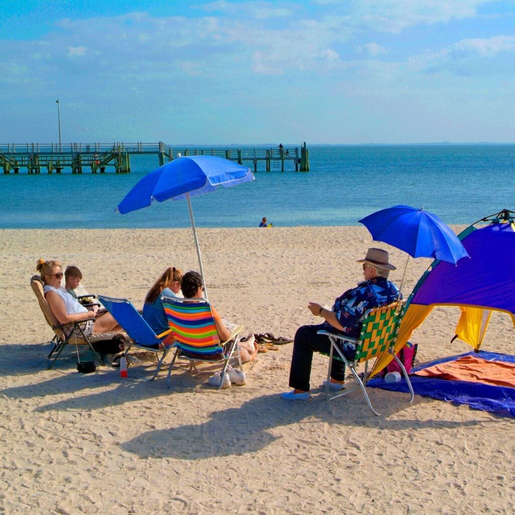 Families relax under colorful umbrellas at Fort DeSoto Beach, enjoying soft sand, calm Gulf waters, and a peaceful, pet-friendly Florida coastal setting.