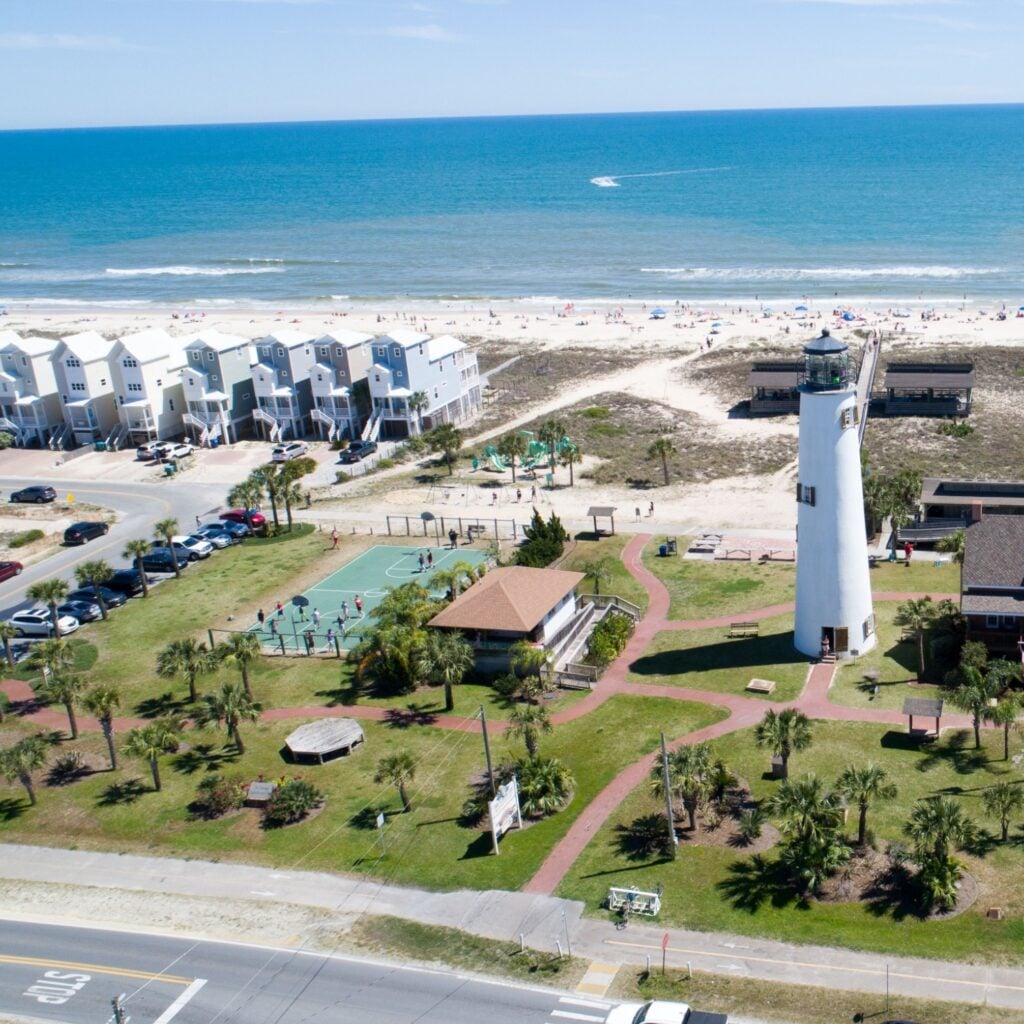 A peaceful view of St. George Island Beach with a lighthouse, palm trees, beach homes, and the Gulf’s calm waters, perfect for a quiet coastal getaway.