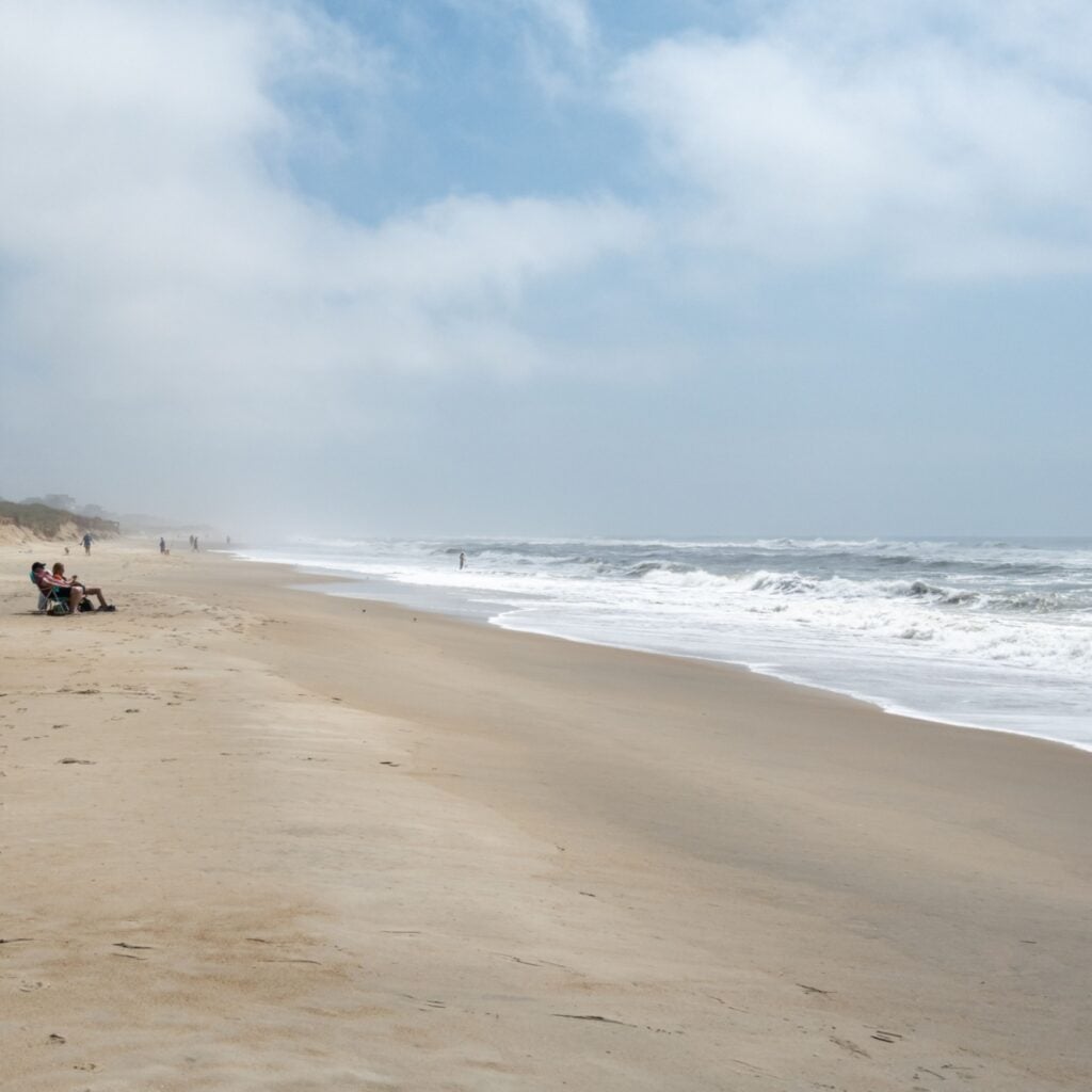 Cape Hatteras, NC, United States - 15 May, 2023: Holiday makers in beach lounger chairs on empty beach watching the waves roll in from the Atlantic Ocean