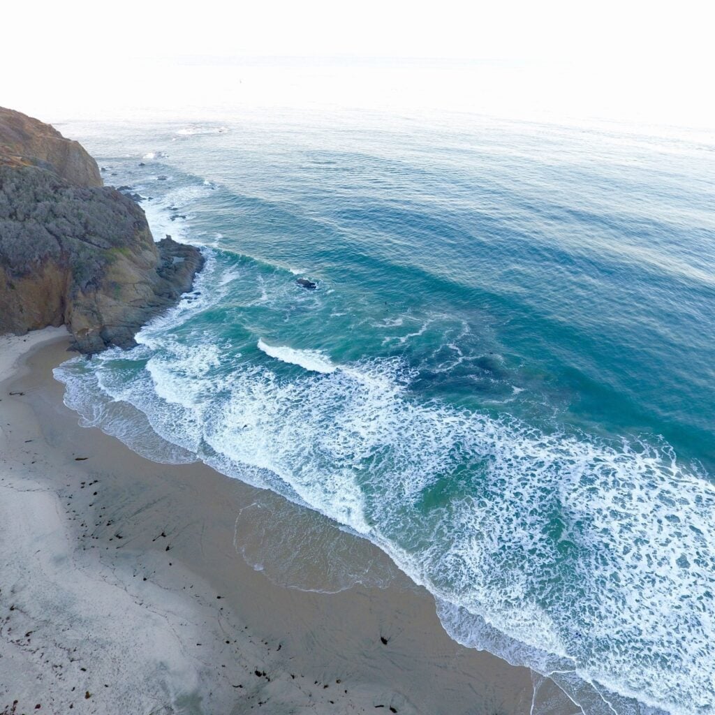 Aerial view of Dana Strands Beach in Dana Point, California, featuring clean sandy shores, gentle waves, and dramatic coastal cliffs. The peaceful setting and turquoise water highlight the beach’s secluded charm, ideal for sunbathing, tide pooling, surfing, and scenic walks along Southern California’s picturesque coastline.