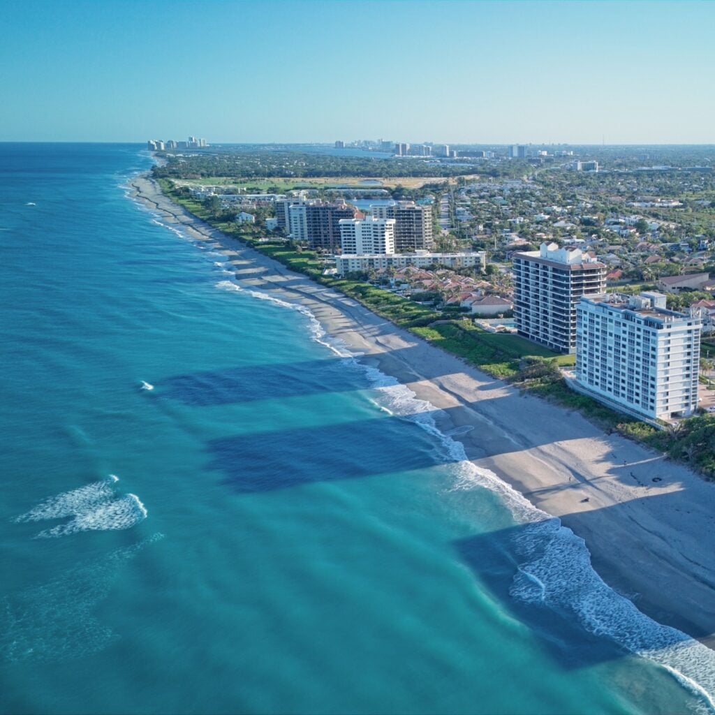 Aerial view of Juno Beach shows clear blue Atlantic waters, soft sandy shore, and peaceful oceanfront buildings, perfect for a quiet Florida coastal escape.