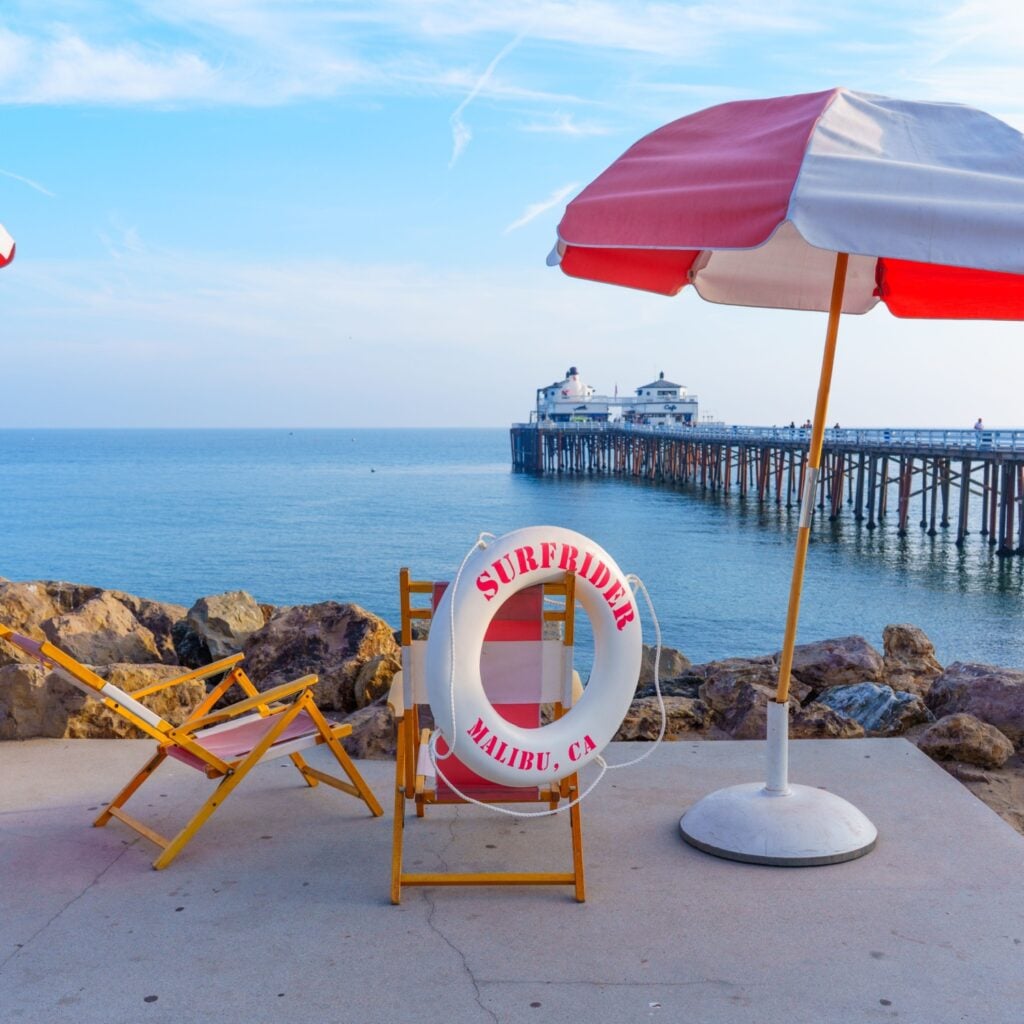 Malibu, California - December 21, 2024: Seating area with lounge chairs and umbrellas by the ocean at Malibu Pier, promoting the Surfrider Hotel.