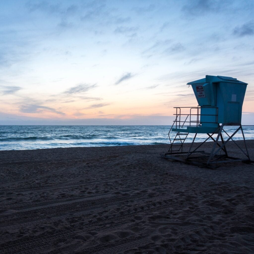 Lifeguard tower at McGrath State Beach in Oxnard, California, set against a peaceful sunset sky and calm ocean waves. The quiet shoreline and soft sand reflect the beach’s rustic charm, offering a serene coastal escape surrounded by nature, dunes, and wetlands.