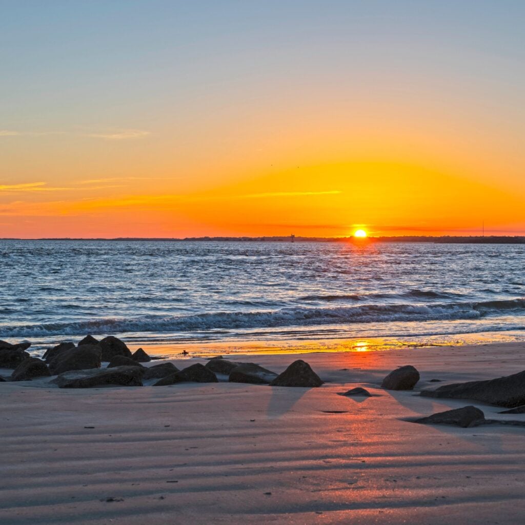 Sunset on Sullivan's Island, SC, with rocks and beach in foreground.