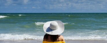 Topsail Beach, NC August 15 2020: Bathing Beauty tan female in yellow bikini sitting in the sand by the ocean