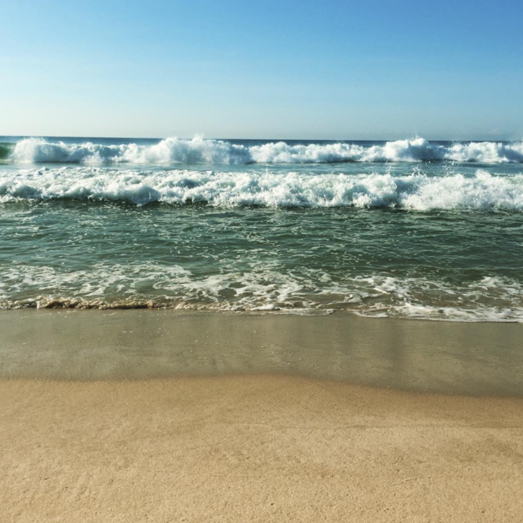 A scenic view of Cupsogue Beach County Park in Westhampton, showing a broad, soft sandy beach with gentle dunes and the blue ocean under a bright sky.