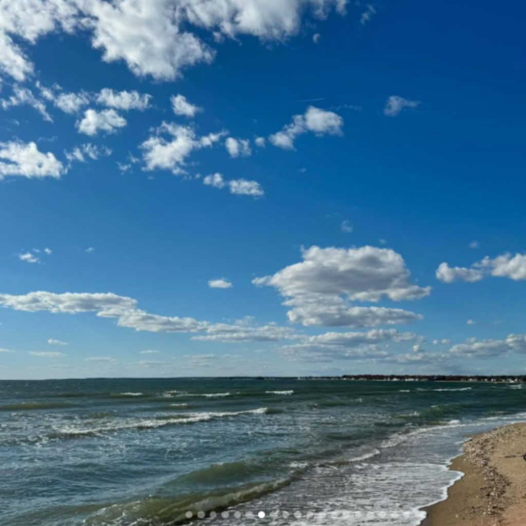 Waves gently roll onto the sandy shoreline at Hammonasset Beach State Park in Madison, CT, under a deep blue sky filled with scattered, fluffy clouds.