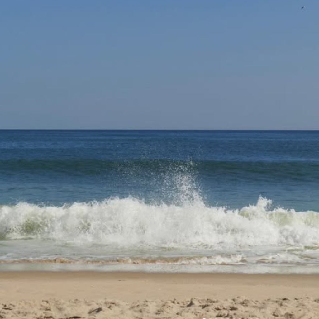 Waves crash onto the golden sand at Sagg Main Beach in Sagaponack, with deep blue Atlantic water and a clear sky creating a bright, peaceful summer scene.